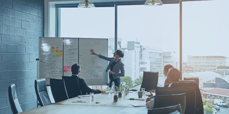 Businesswoman presenting at a whiteboard during a meeting in a modern conference room.