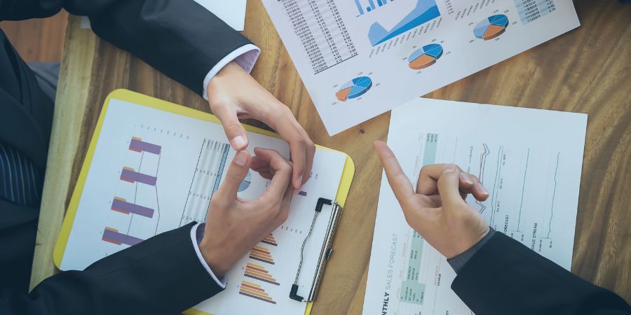 Business professionals discussing financial charts and graphs on a table with clipboards and documents.